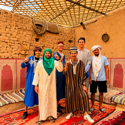 Groepsfoto van 22-35ers reis Marokko in traditionele kleding in een kasbah, op kleurrijke tapijten.