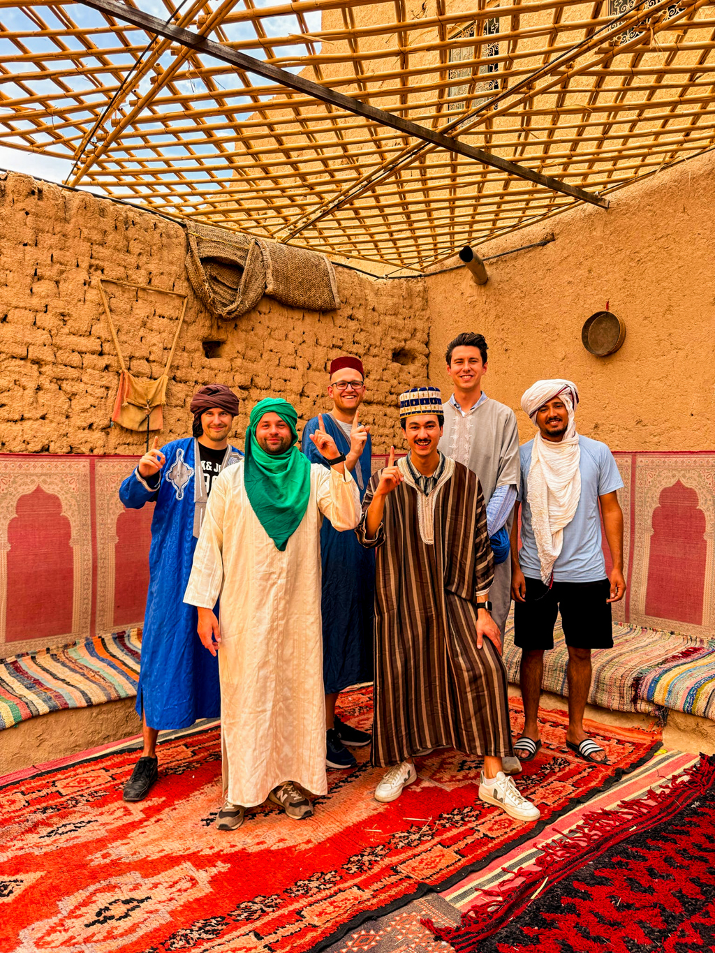 Groepsfoto van 22-35ers reis Marokko in traditionele kleding in een kasbah, op kleurrijke tapijten.