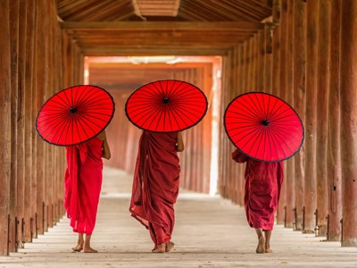 Monniken met rode parasols lopen door een houten gang in Myanmar.