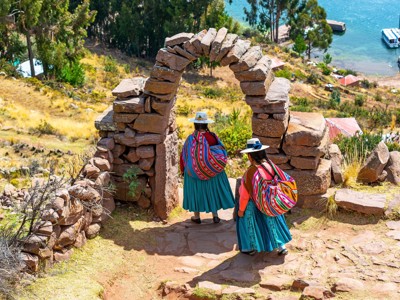 Twee vrouwen in traditionele kleding lopen door een stenen boog bij het Titicacameer in Peru.