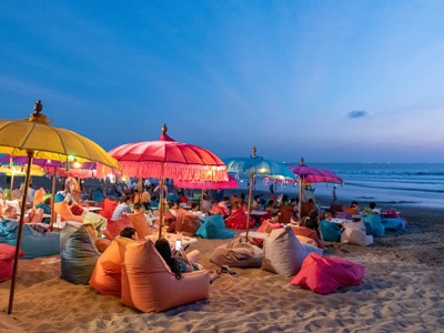 Gezellige strandbar op Bali bij zonsondergang met kleurrijke parasols en zitzakken aan zee.