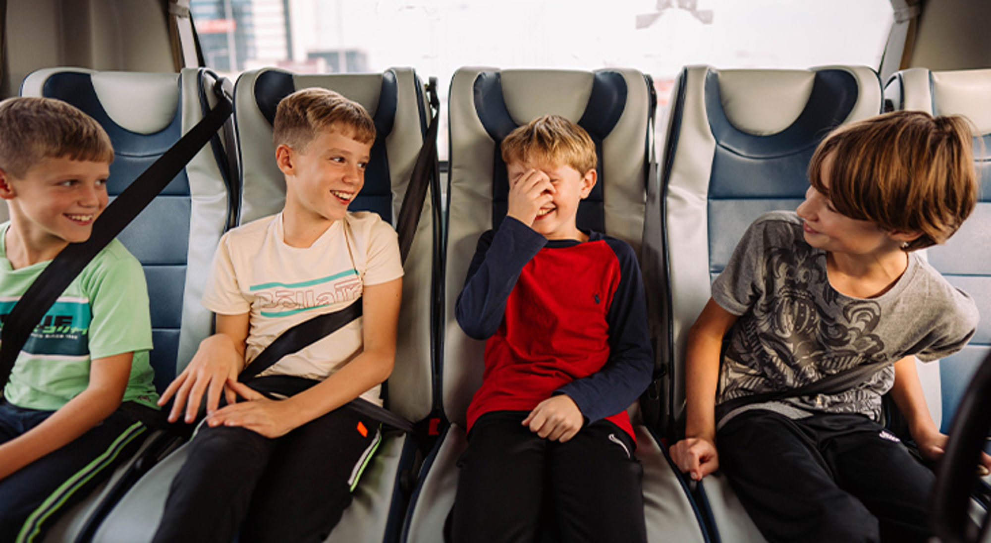 Vier kinderen lachen op de achterbank in de auto, vastgemaakt met veiligheidsgordels.