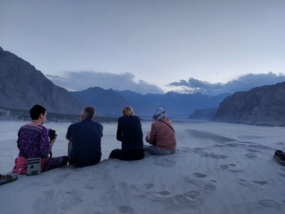 Reizigers zitten op zandduinen en kijken uit over de bergen van Baltistan en Hunza in Pakistan bij zonsondergang.
