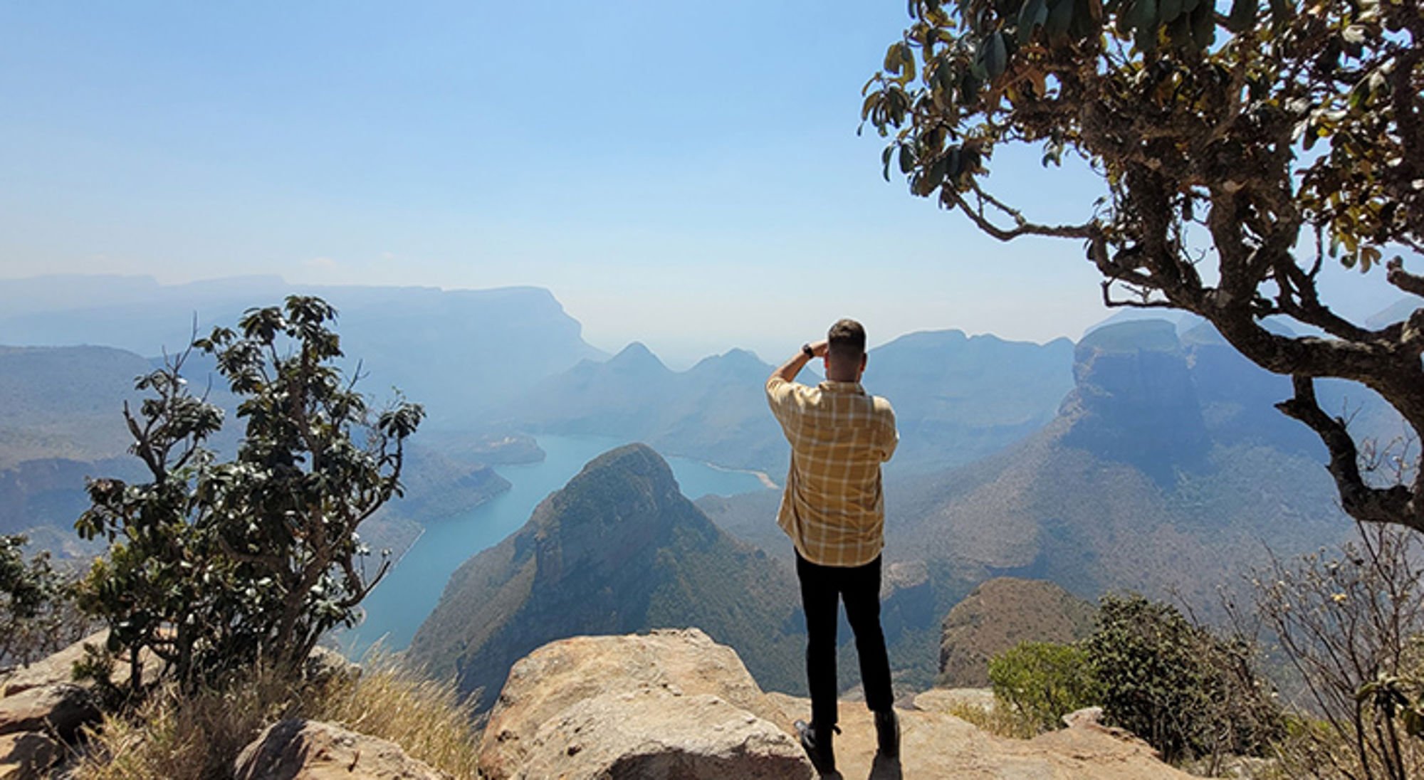 Ethan in Zuid-Afrika Man op uitkijkpunt met panoramisch uitzicht op een rivierkloof en bergen.