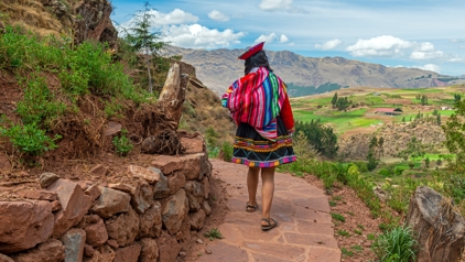 Vrouw in traditionele kleding wandelt over een bergpad met uitzicht op de Andesvallei in Peru.
