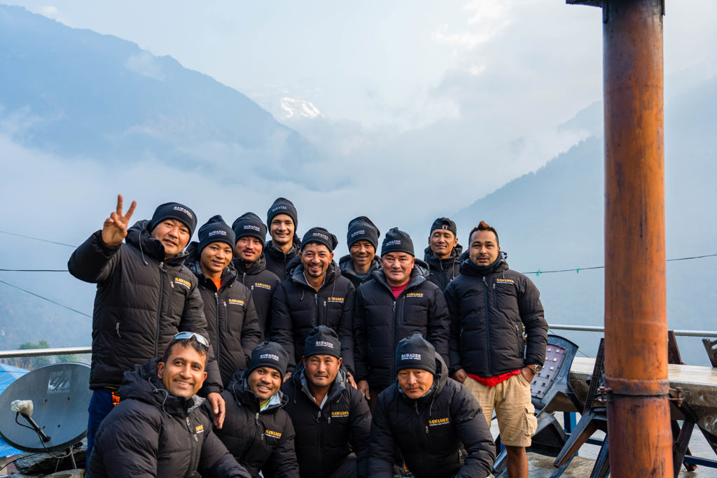 Groepsfoto van lokale gidsen tijdens een 22-35ers reis Nepal, met mistige bergen op de achtergrond.