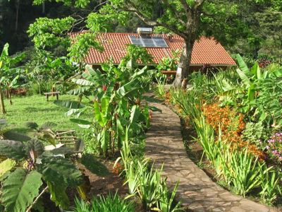 Pad door tropische tuin naar lodge met rood dak en zonnepanelen tijdens Route Nicaragua, 23 dagen.