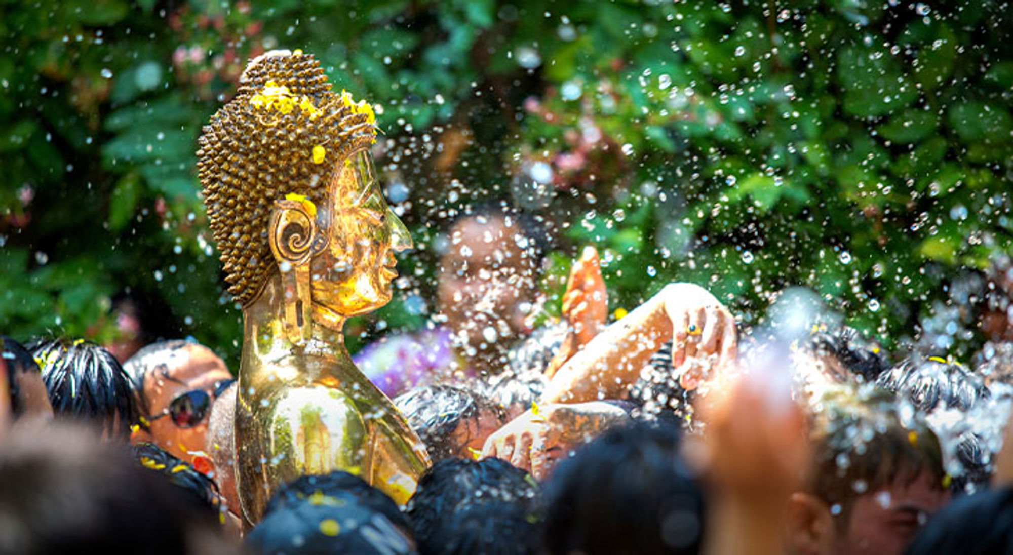 Songkran Thailand Gouden Boeddhabeeld tussen feestvierders tijdens het waterfestival, met opspattend water op de voorgrond.