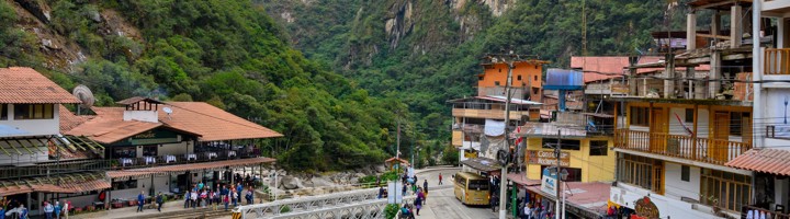Straatbeeld van Aguas Calientes in Peru met brug over de rivier en beboste bergen op de achtergrond.