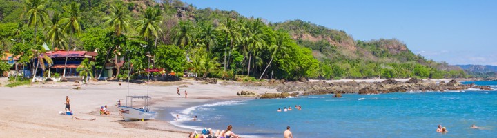 Zandstrand bij Montezuma, Costa Rica, met palmbomen, rotsen en zwemmers in een rustige baai.