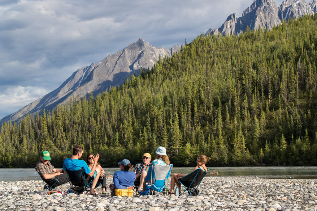 Groep reizigers ontspant aan een rivier met bergen en naaldbos op de achtergrond, tijdens groepsrondreis Canada West.