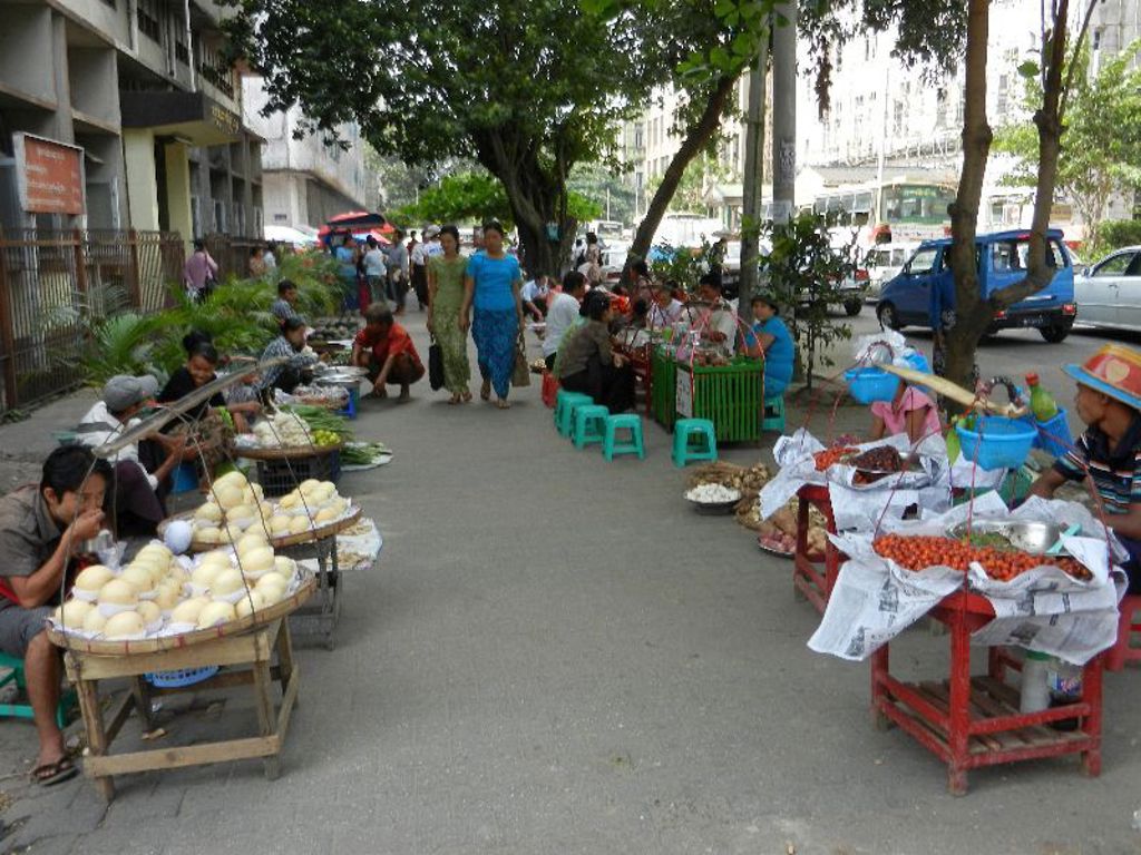 Straatmarkt in Myanmar met verkopers en kramen vol fruit en groenten langs de stoep.