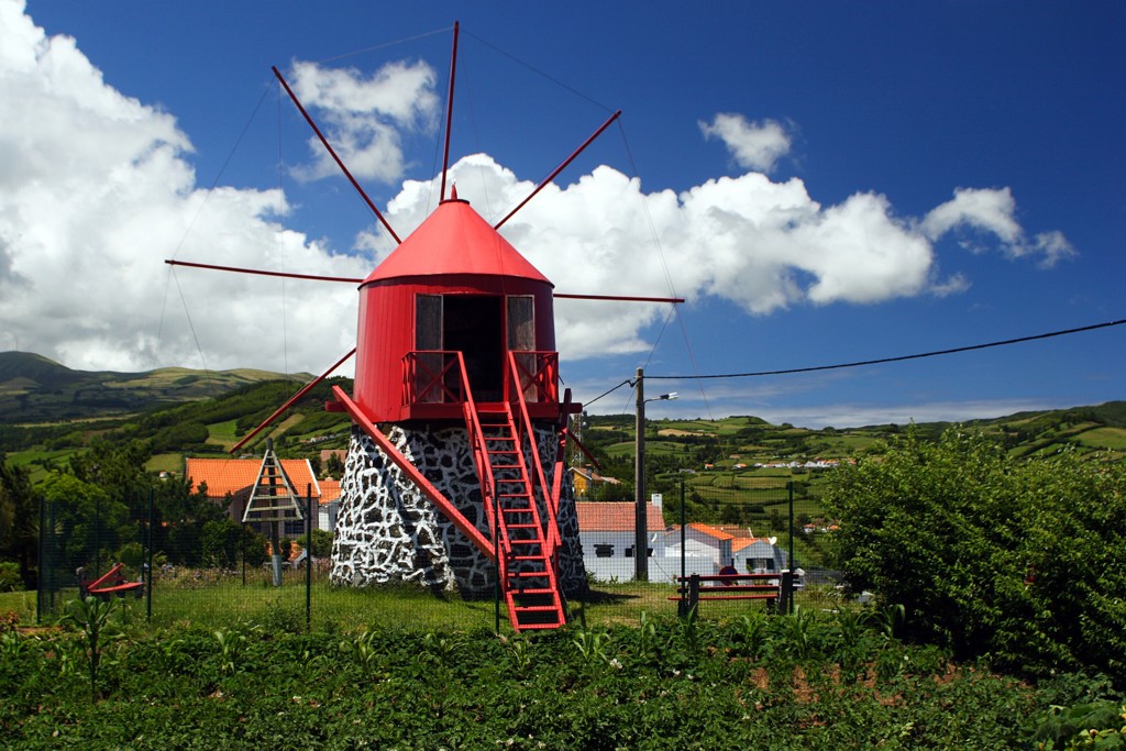 Rode windmolen op de Azoren met groen heuvellandschap en wolkenlucht op de achtergrond.