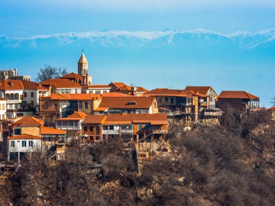 Huizen met rode daken en kerktoren in Sighnaghi, Georgië, met besneeuwde Kaukasus op de achtergrond.