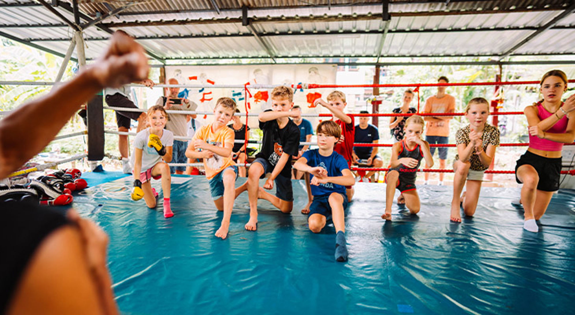 Kinderen trainen muay thai in een boksring, met een trainer op de voorgrond.