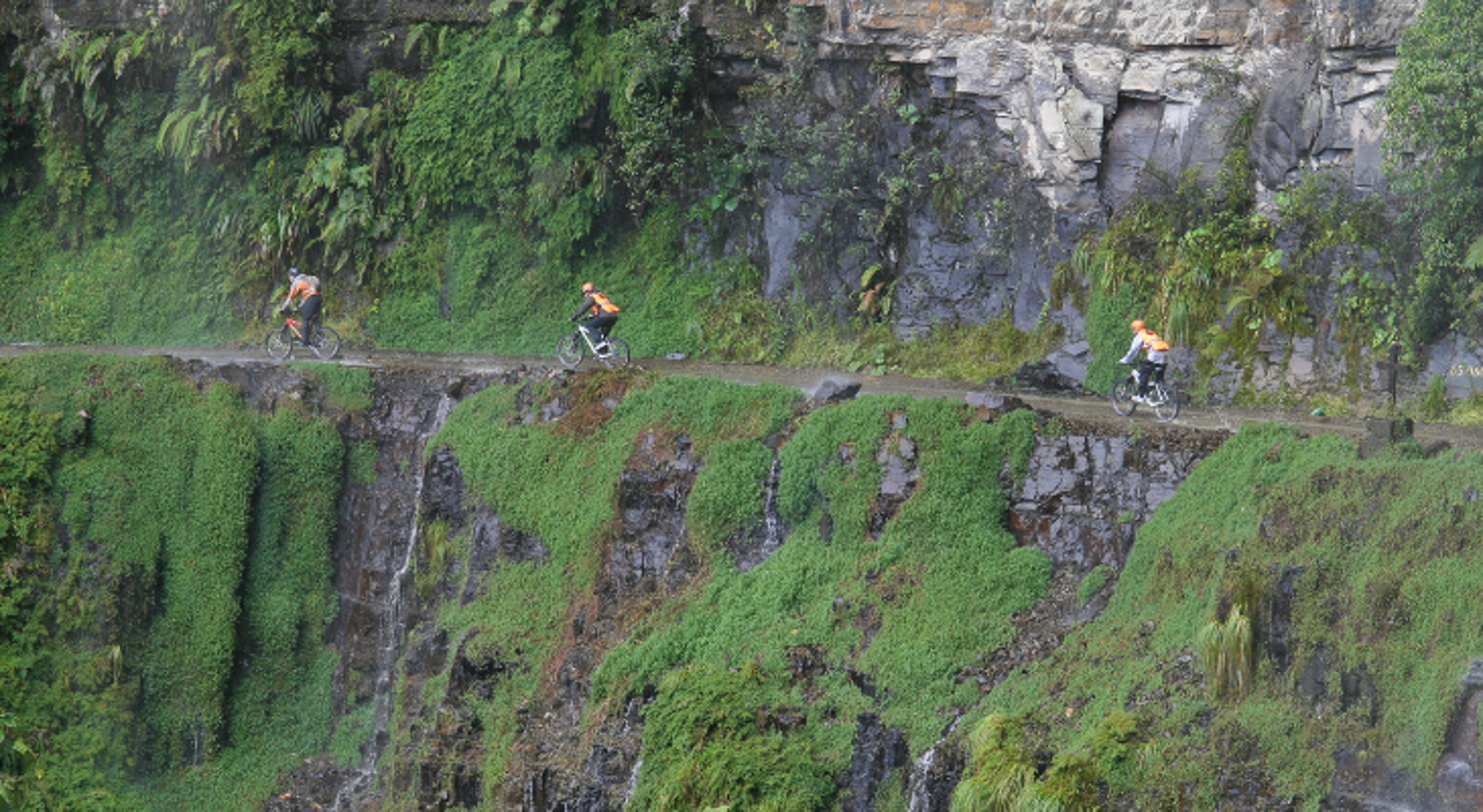 Wandelen Death Road Mountainbikers op de Yungas Road (Death Road) langs een steile, groene rotswand in Bolivia.