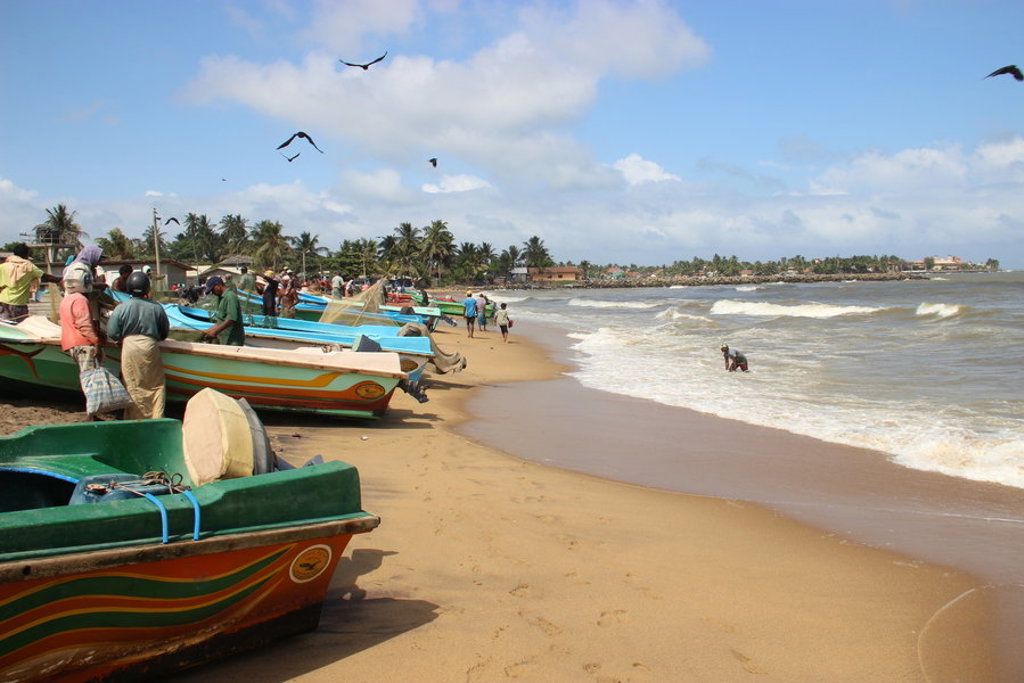 Vissersboten op het strand aan de kust van Sri Lanka, met palmbomen en golven op de achtergrond.