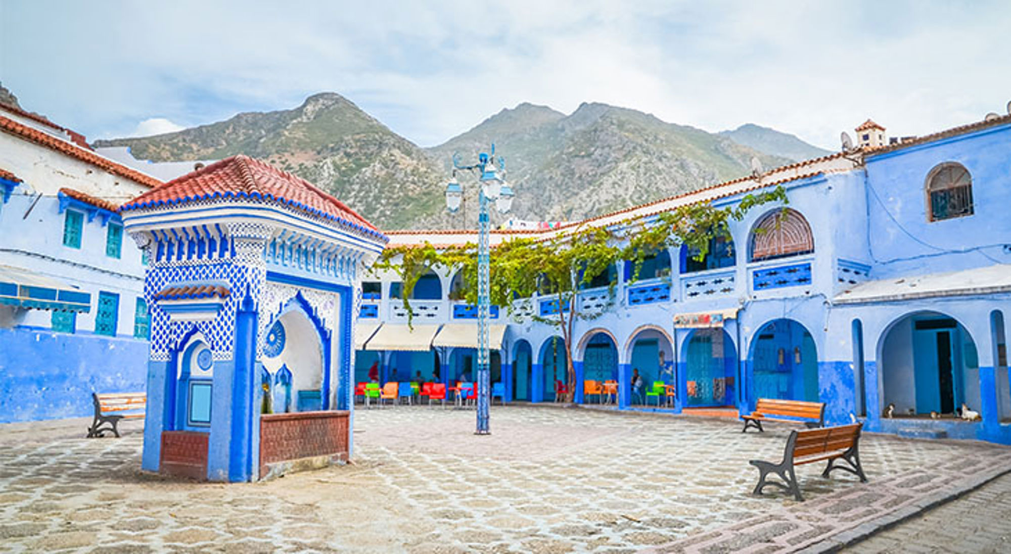 Chefchaouen Blauw-witte binnenplaats met mozaïekfontein in Chefchaouen, Marokko, met het Rifgebergte op de achtergrond.