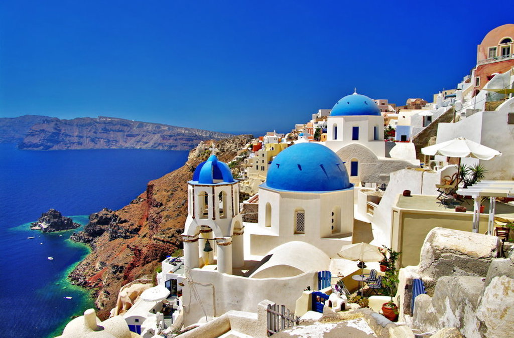 Witte huizen en blauwgekleurde koepelkerken in Oia op Santorini, met uitzicht op de caldera en de Egeïsche Zee.
