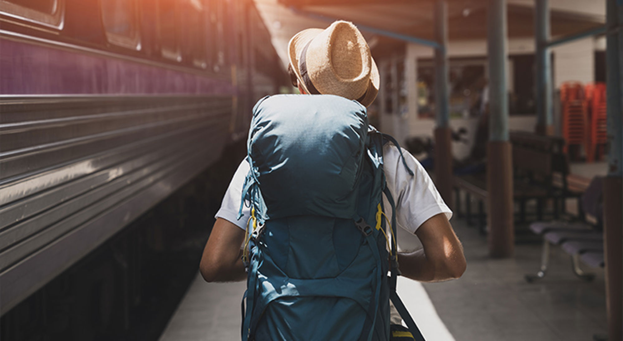Rugzaktoerist met hoed loopt over een perron langs een trein.