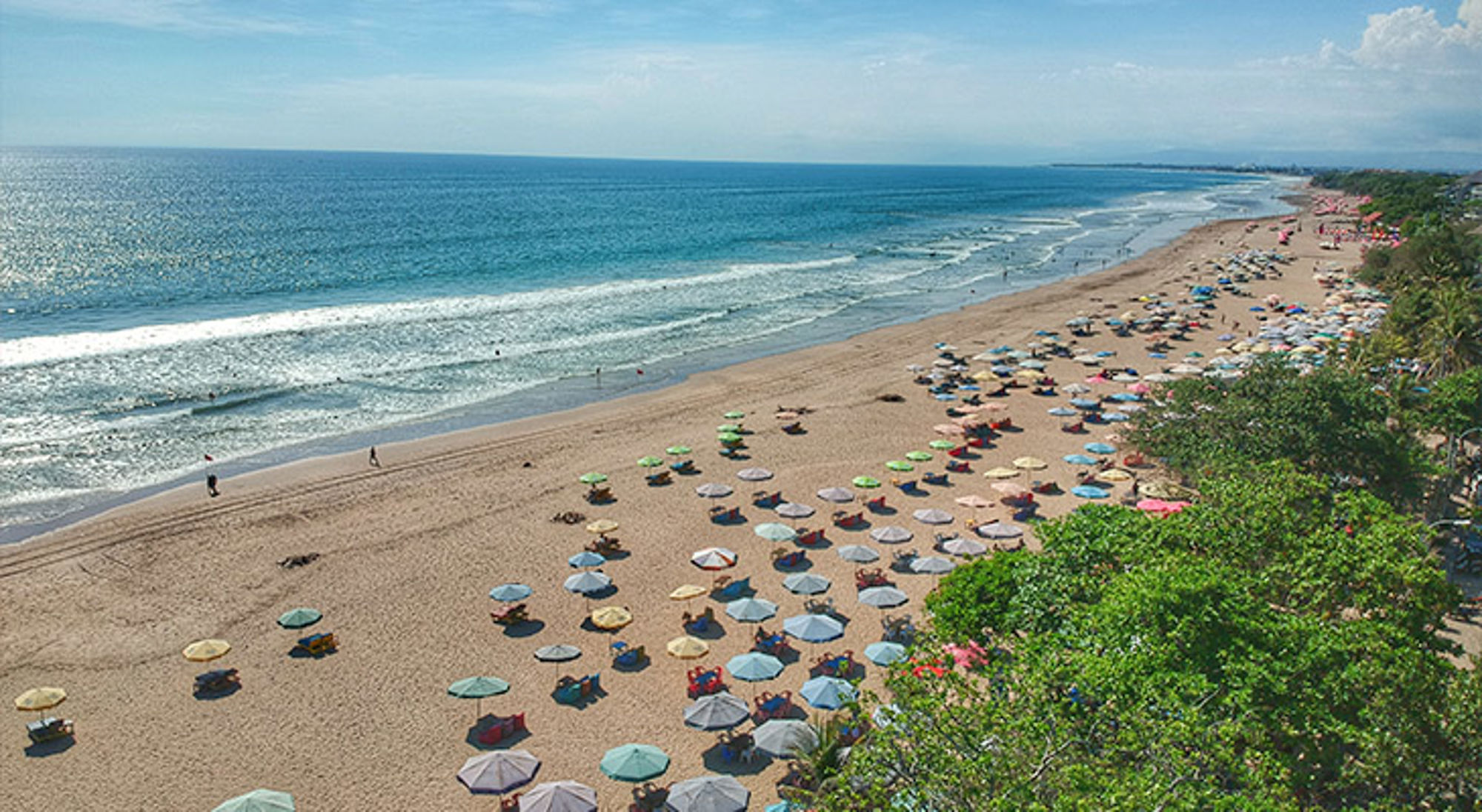 Seminyak Beach Panoramisch uitzicht op een lang zandstrand met kleurrijke parasols en zachte golven langs de kust.