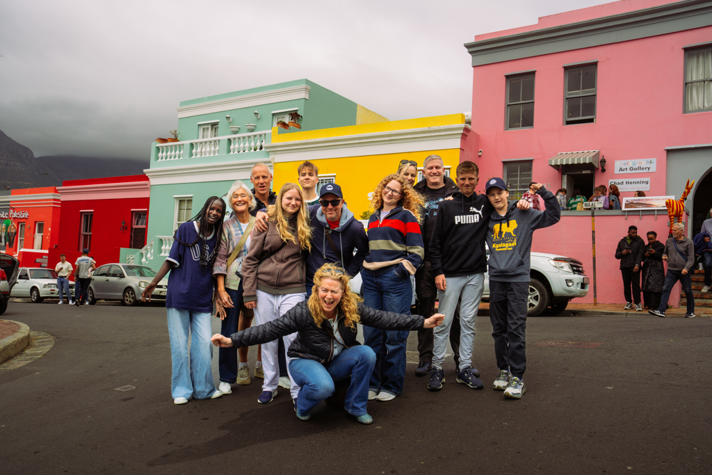 Groep reizigers poseert in Bo-Kaap, Kaapstad, voor kleurrijke huizen tijdens familiereis Zuid-Afrika Tuinroute & Kruger.