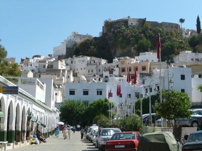 Straat in Chefchaouen met witgekalkte huizen op de heuvel en Marokkaanse vlaggen langs de weg.