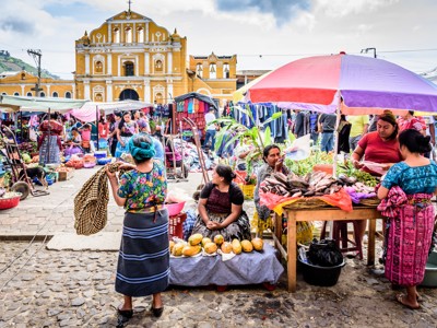 Markt in Guatemala met kraampjes onder parasols en de gele kerk op de achtergrond.