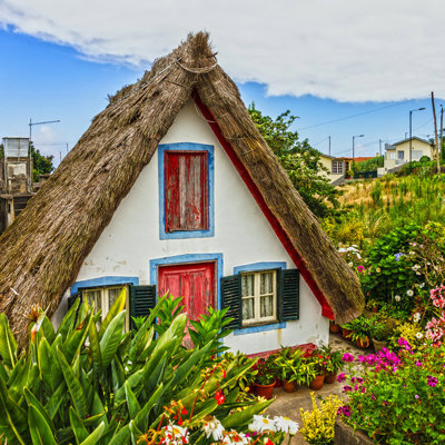 Traditioneel Madeirees huisje met rieten dak en kleurrijke luiken, omringd door bloemen en groen op Madeira.