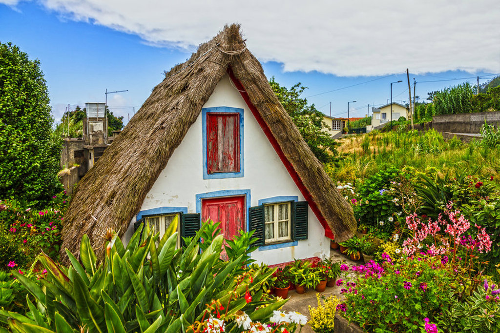 Traditioneel Madeirees huisje met rieten dak en kleurrijke luiken, omringd door bloemen en groen op Madeira.