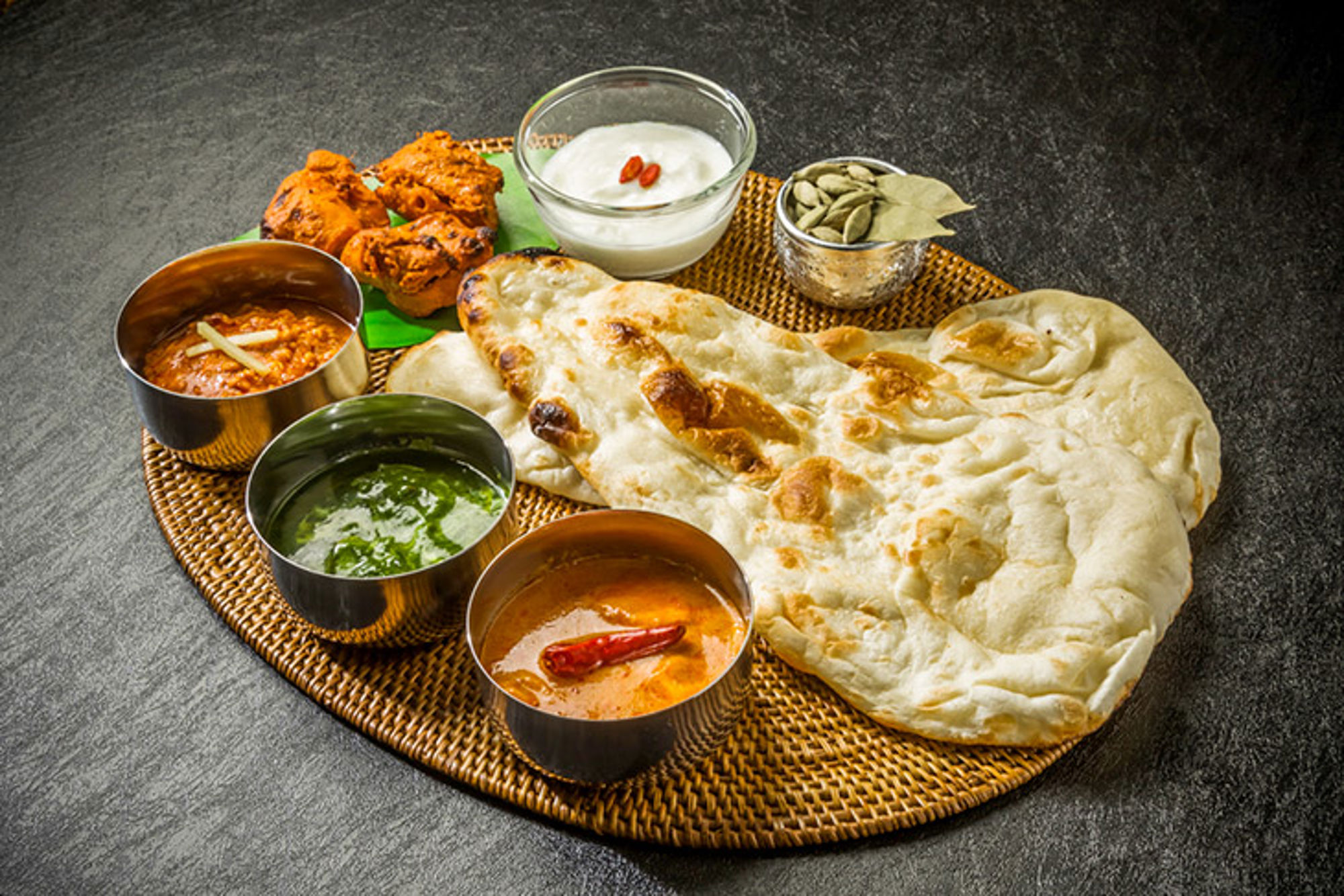 Eten, India Indiase thali met naan, curry’s, chutneys en yoghurt op een rieten schaal.