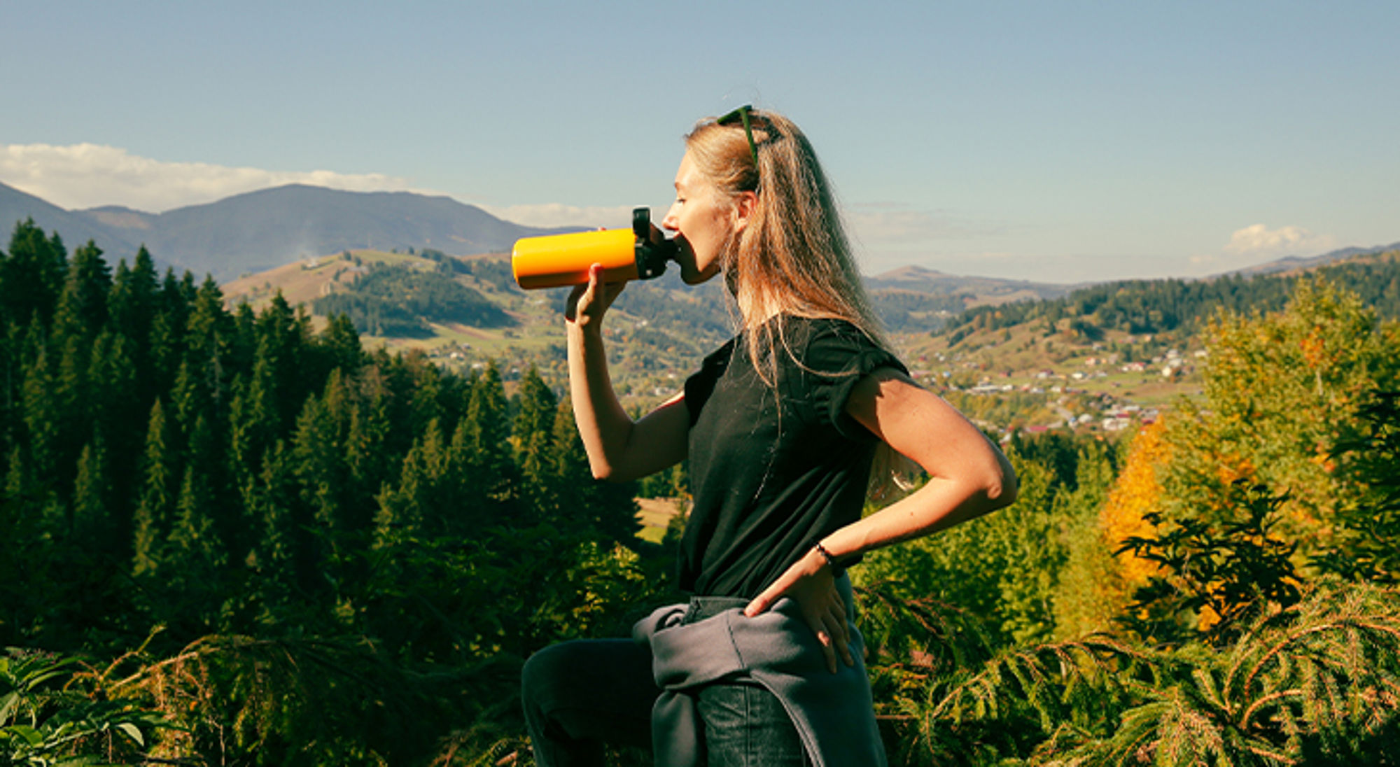 Waterfles op reis Wandelaar drinkt uit een fles met uitzicht op groene bergen en een vallei.