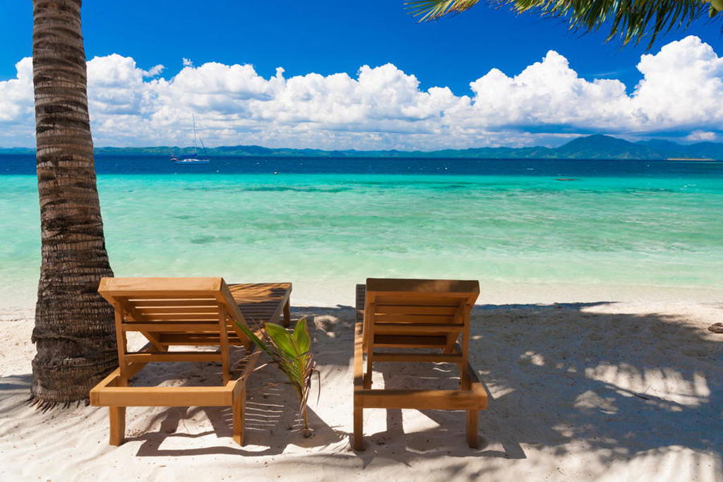Strand met ligstoelen onder palmbomen aan turquoise zee tijdens een groepsrondreis door de Filipijnen.