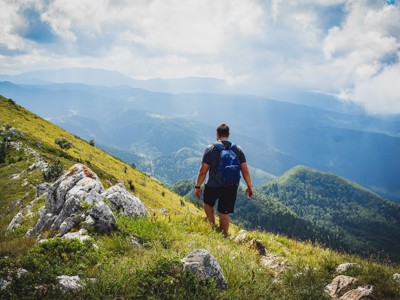 Wandelaar met rugzak op bergpad met uitzicht over groene heuvels in Bosnië & Herzegovina.