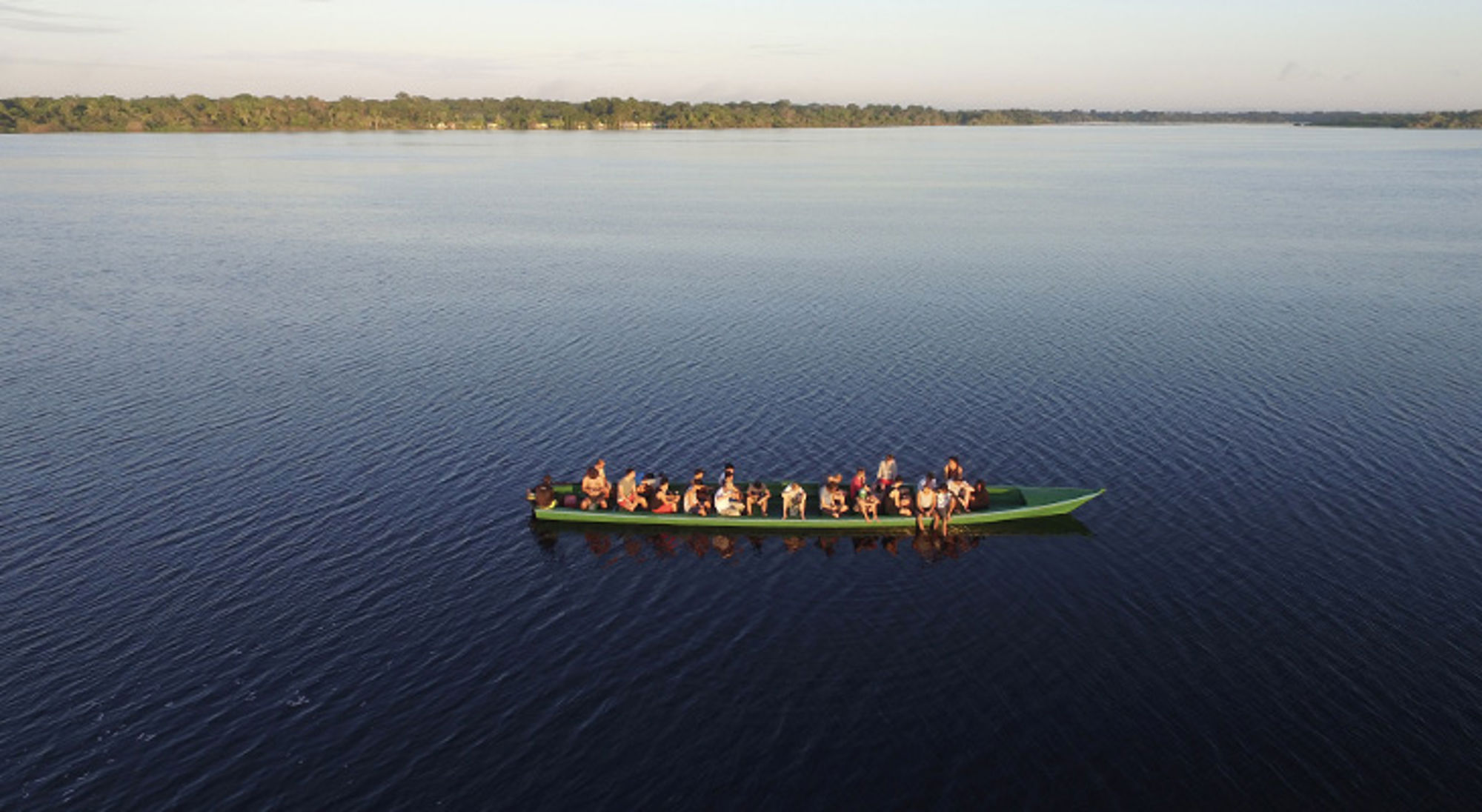 boottocht over de amazone Groep reizigers in een lange kano op een rustige rivier, met bosrijke oever op de achtergrond.