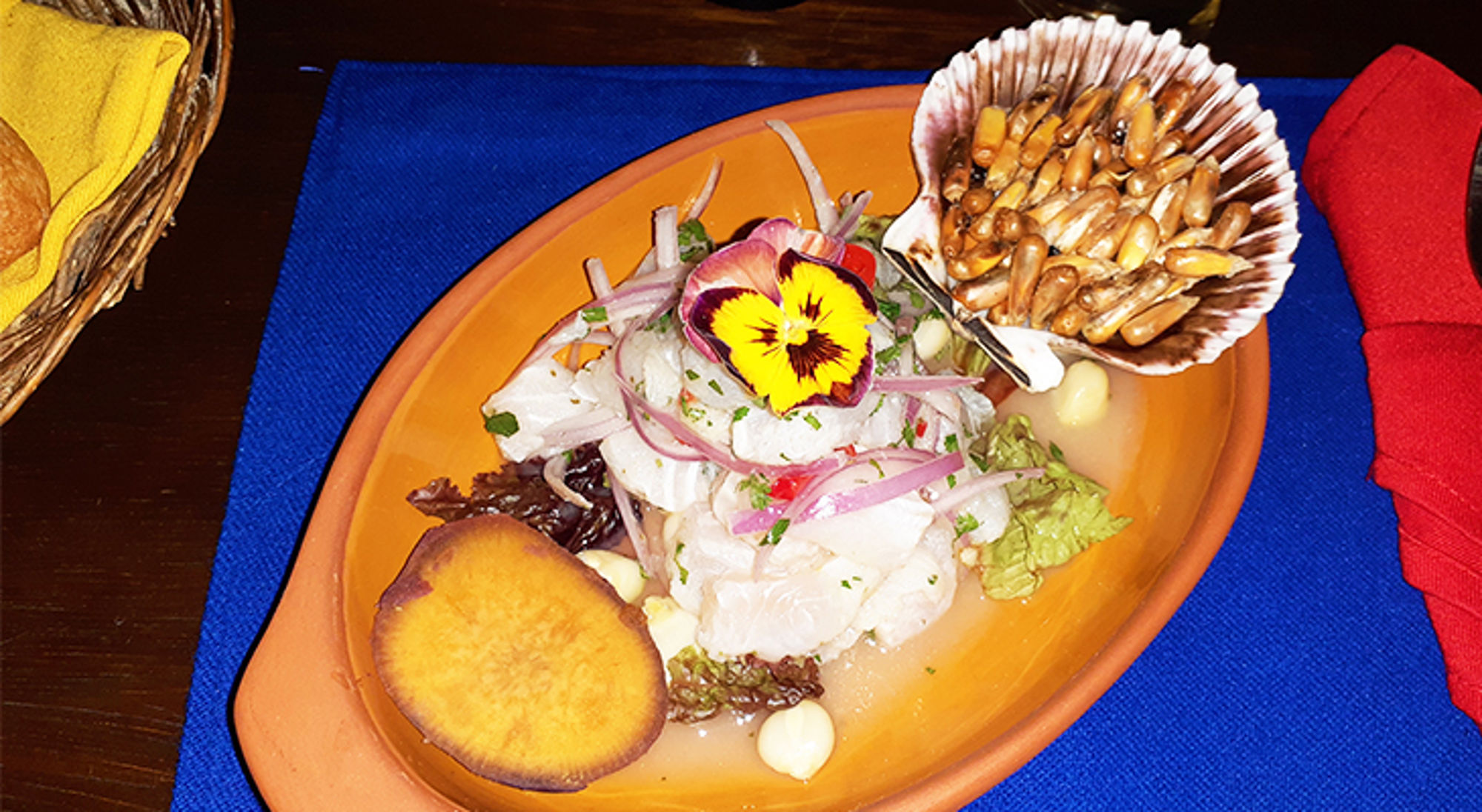Ceviche met rode ui, eetbare bloem en maïs geserveerd op een bord.