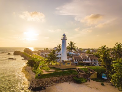 Vuurtoren van Galle bij zonsondergang aan de kust van Sri Lanka, omringd door palmbomen en koloniale gebouwen.