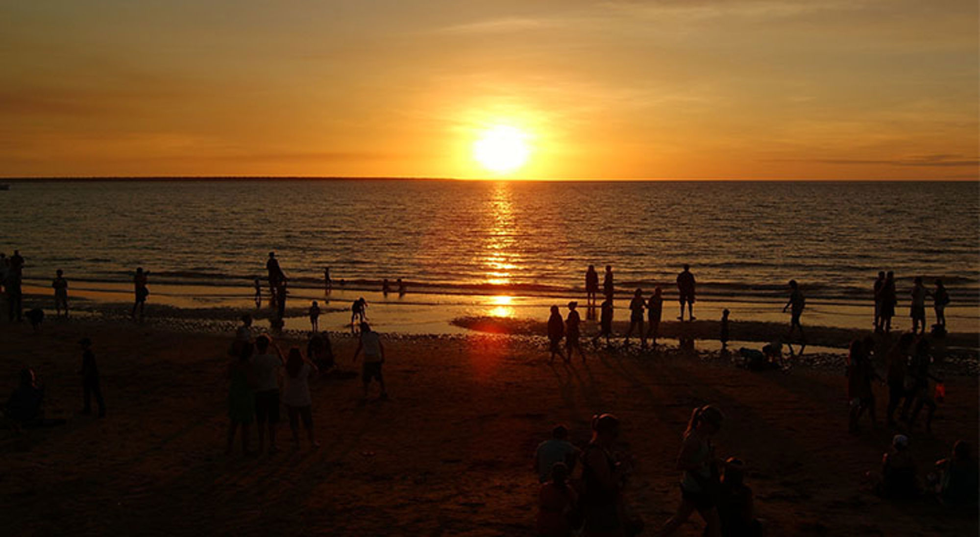 Zonsondergang boven zee met silhouetten van mensen op het strand.