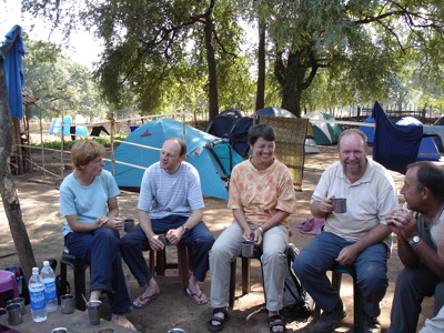 Reisgroep op camping in Orissa, zittend bij tenten en drinkend uit metalen bekers.