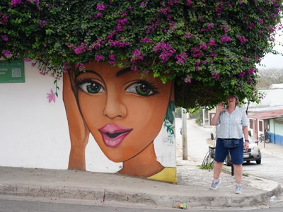 Muurschildering van een vrouwenportret onder bougainvillea in een straat in Nicaragua.
