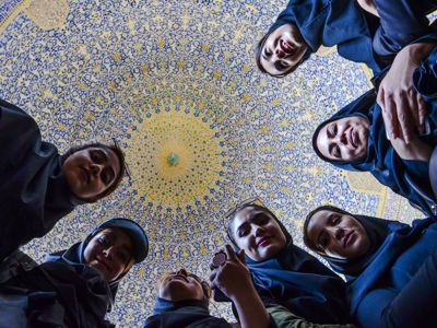 Vrouwen kijken omlaag in een koepel met blauw-geel mozaïek, tijdens de 19-daagse route door Iran.