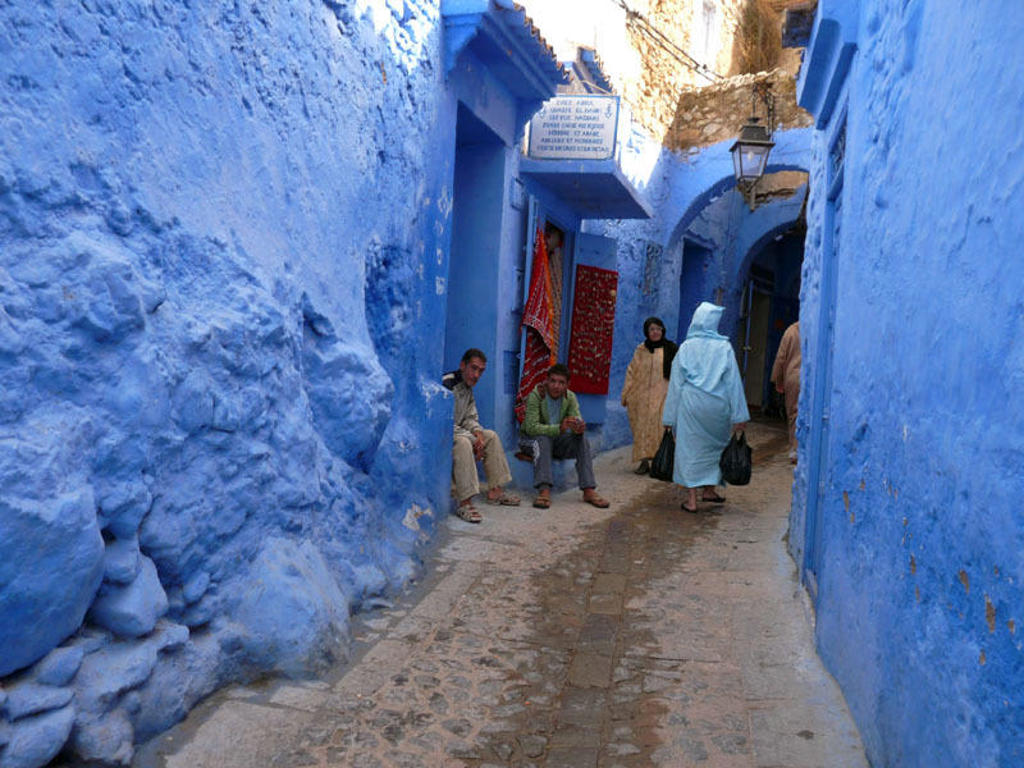 Blauwe steeg in Chefchaouen, Marokko, met bewoners en wandelaars tussen de beschilderde huizen.