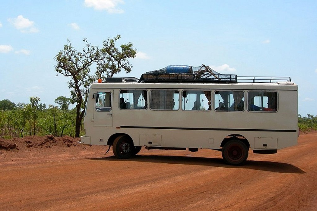 Witte reisbus op een rode zandweg tijdens een groepsrondreis door Ghana, Togo en Benin.