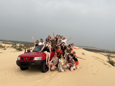 Groep reizigers poseert bij rode jeep op zandduinen tijdens de Route Vietnam.