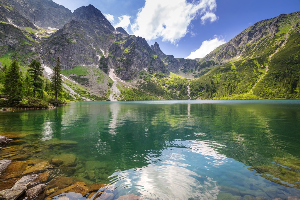 Bergmeer in het Tatragebergte in Polen met groene hellingen en rotsige toppen onder een blauwe lucht.