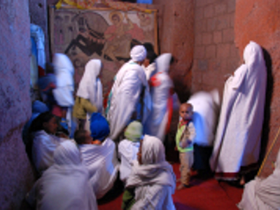 Pelgrims in witte gewaden bij een Ethiopisch-orthodoxe kerk, met religieuze muurschildering op de achtergrond.