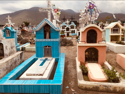 Kleurrijke graven op een begraafplaats in Peru, met bergen op de achtergrond.