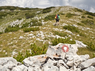Wandelaar met rugzak volgt rood-witte route markering door berglandschap in Bosnië tijdens Route Bosnië, 8 dagen.