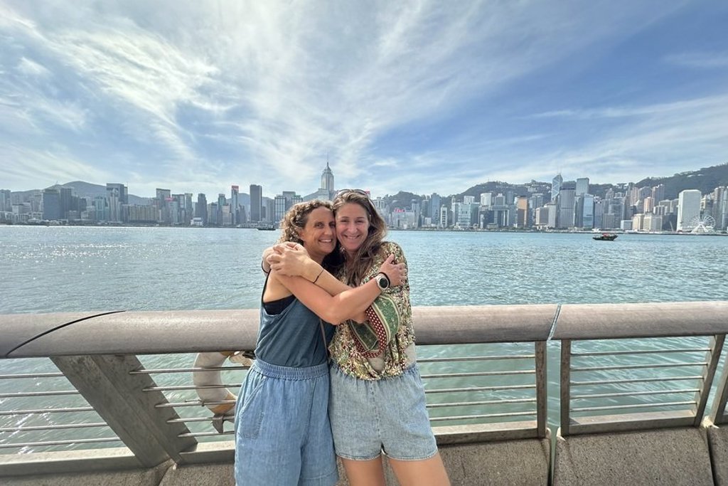 Twee reizigers omhelzen elkaar aan de Victoria Harbour met de skyline van Hongkong op de achtergrond.