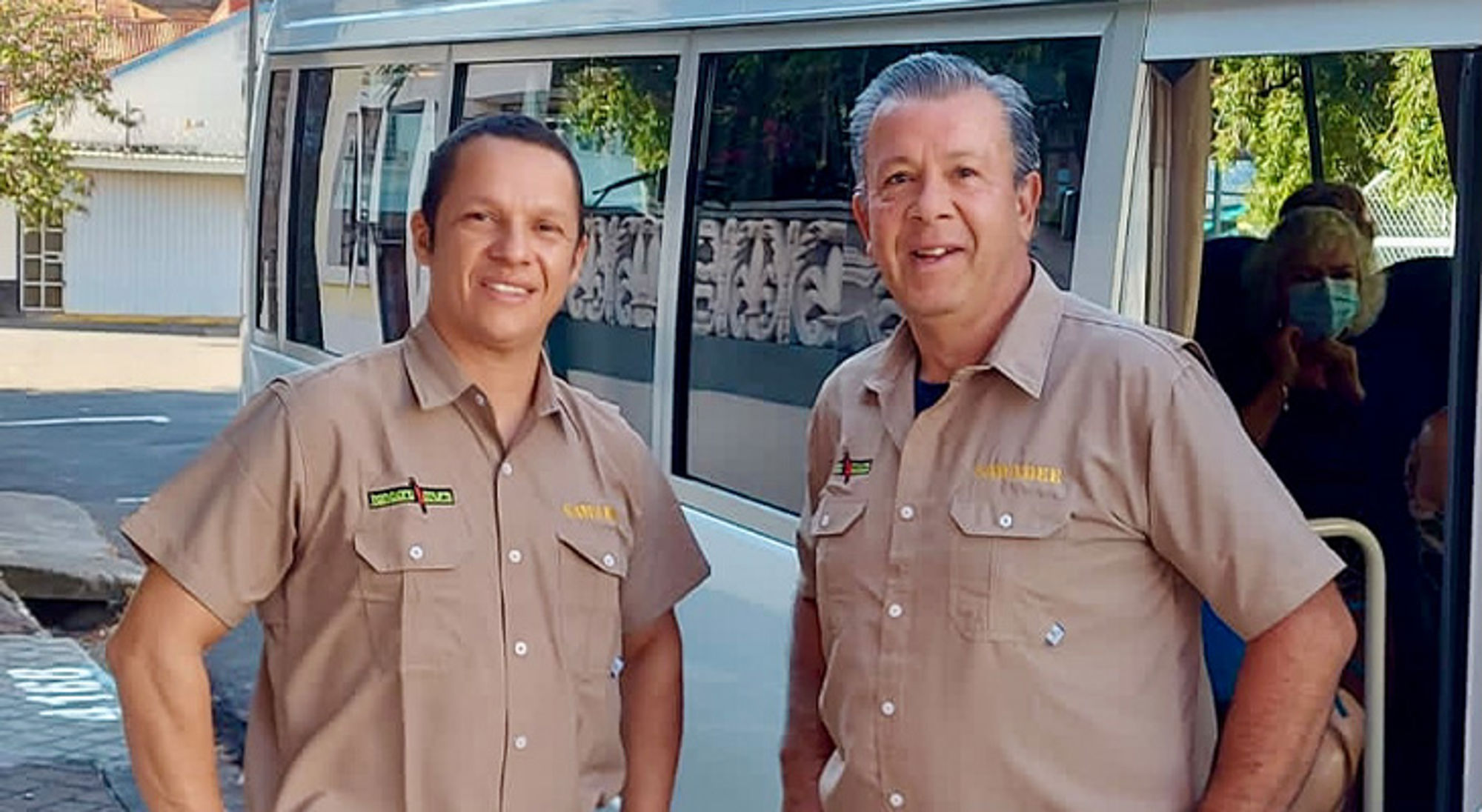 Twee medewerkers in uniform staan voor een shuttlebus bij een hotel.